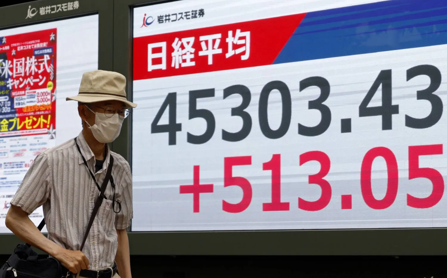 أحد المشاة يعبر الطريق أمام شاشة تعرض حركة الأسهم في العاصمة اليابانية طوكيو (إ.ب.أ)