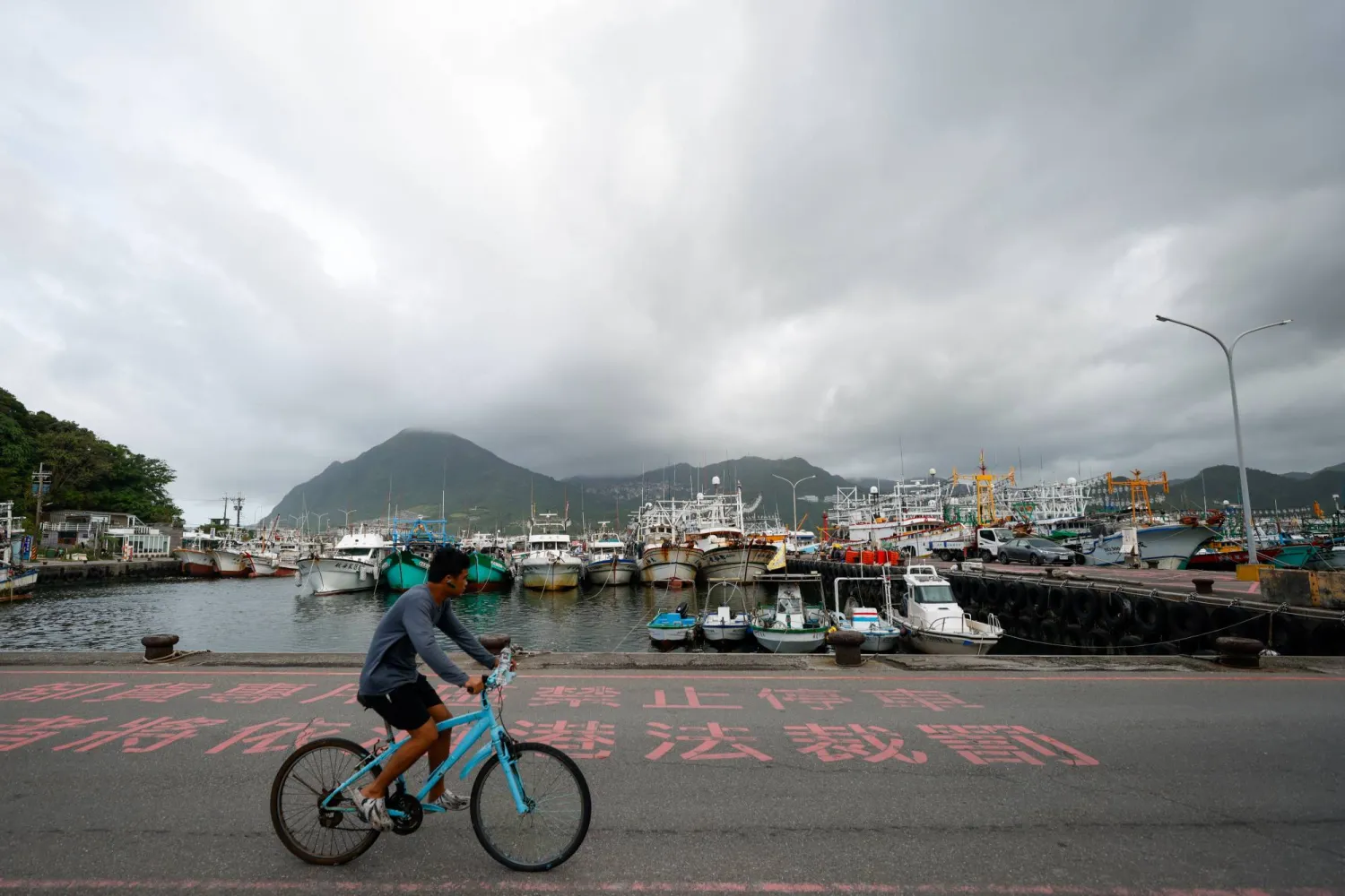 شخص يقود دراجة هوائية أمام قوارب الصيد الراسية في تايوان (إ.ب.أ)