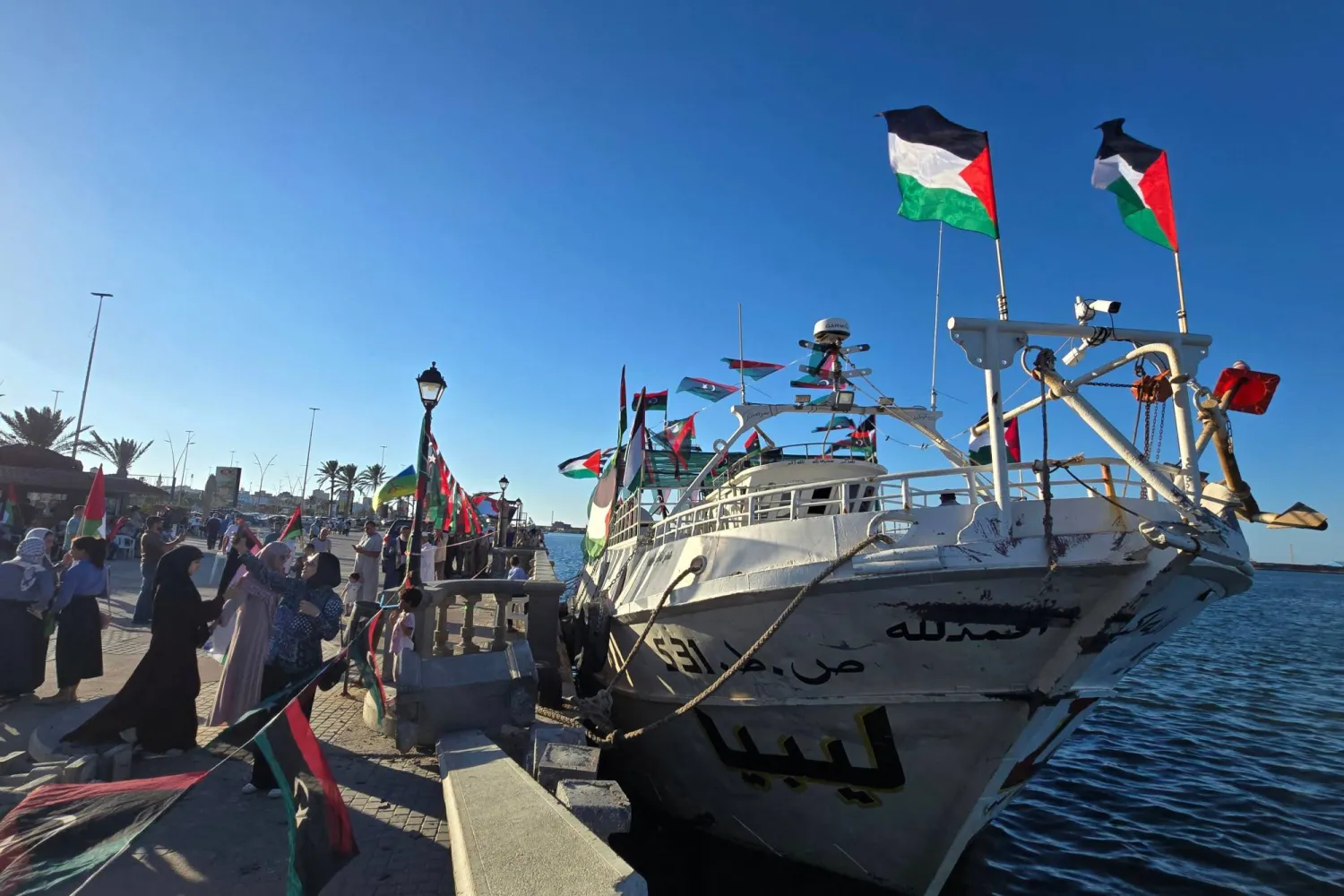 People pose for a picture in front of the Omar al-Mukhtar ship, a Libyan ship setting sail on September 17 to join the Global Sumud Flotilla, at the port in Tripoli on September 16, 2025. (Photo by Mahmud Turkia / AFP)