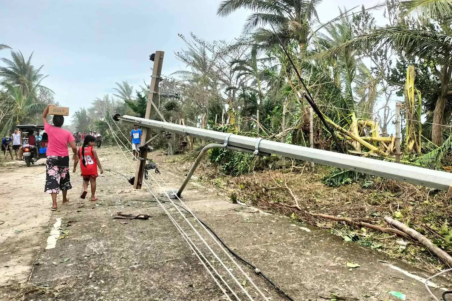 TOPSHOT - Residents walk past a fallen electric post along a road in Calayan island, Cagayan province on September 23, 2025, a day after Super Typhoon Ragasa hit the island. (Photo by Cristy Gaffud / AFP)