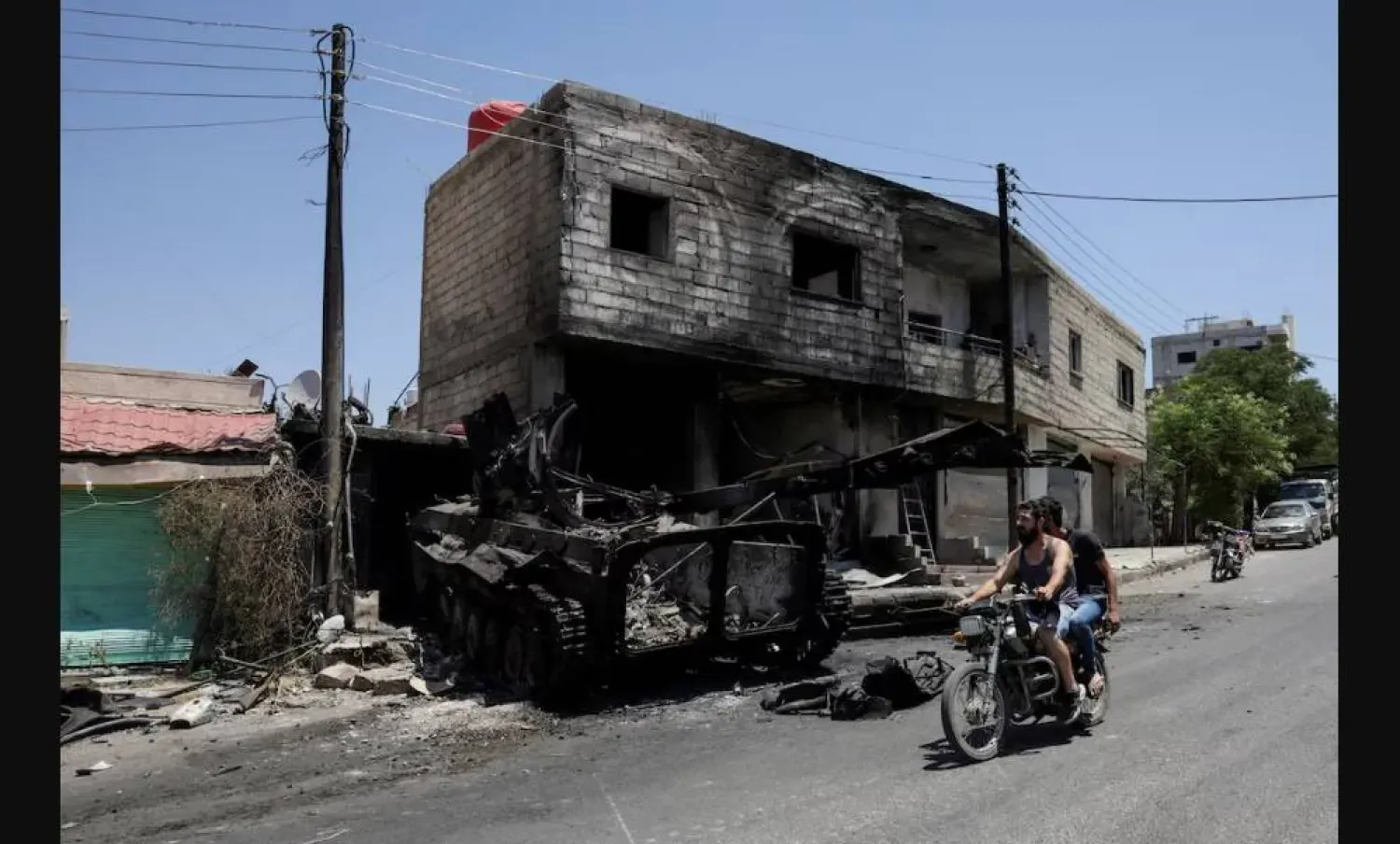 Suriye'nin Dürzi çoğunluklu Süveyda kentinde çıkan ölümcül çatışmaların ardından iki kişi yanan bir askeri aracın önünde motosikletle geçiyor (Reuters)