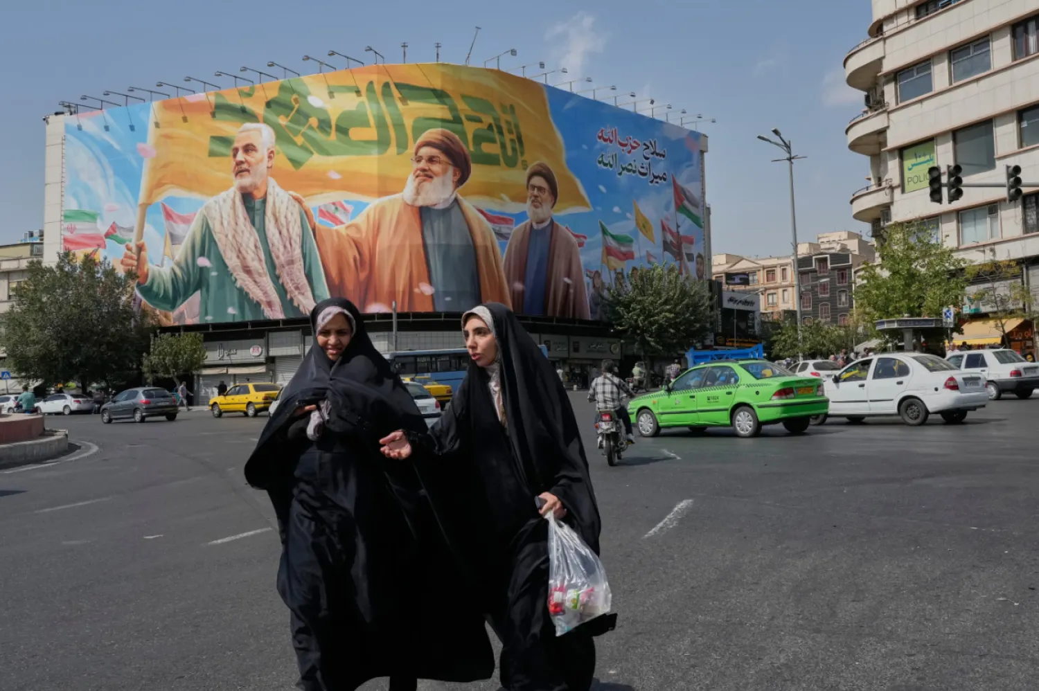 Two women walk past a huge banner showing the late commander of the Iran's Revolutionary Guard expeditionary Quds Force, Gen. Qassem Soleimani, who was killed in a US drone attack in 2020, and two late Hezbollah leaders Hassan Nasrallah, center, and Hashem Safieddine, who were killed in Israeli airstrikes in 2024, at the Enqelab-e-Eslami (Islamic Revolution) square, in Tehran, Iran, Saturday, Sept. 27, 2025.  (AP Photo/Vahid Salemi)