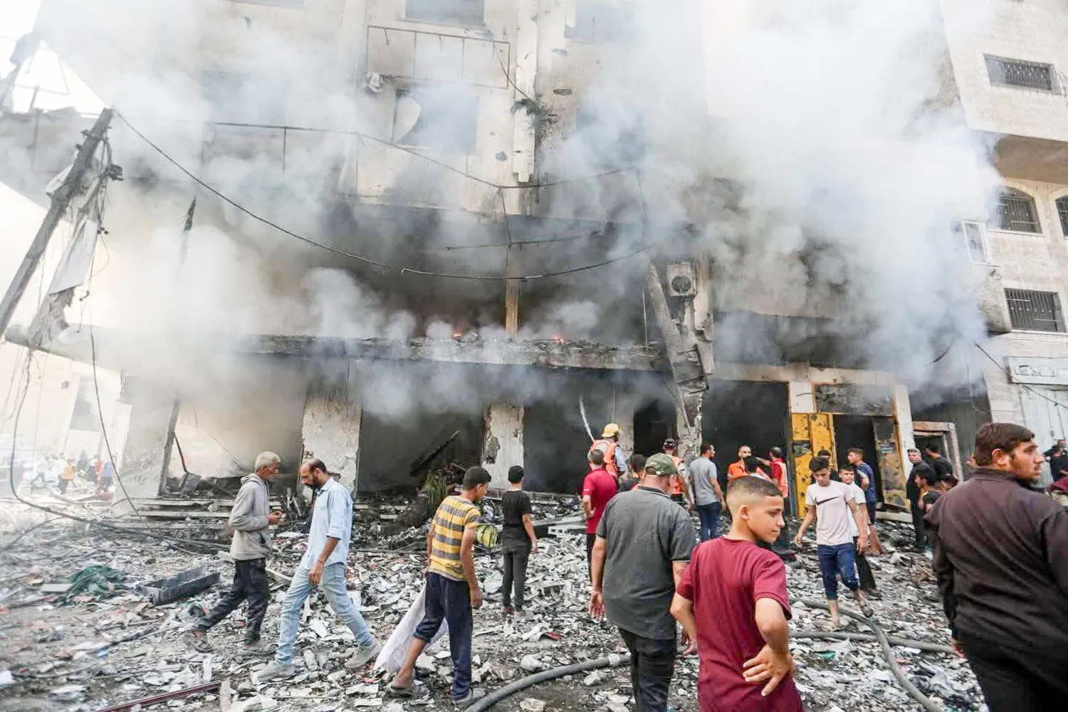 فلسطينيون خارج مبنى تضرر بغارة جوية إسرائيلية يوم الأحد (د.ب.أ)