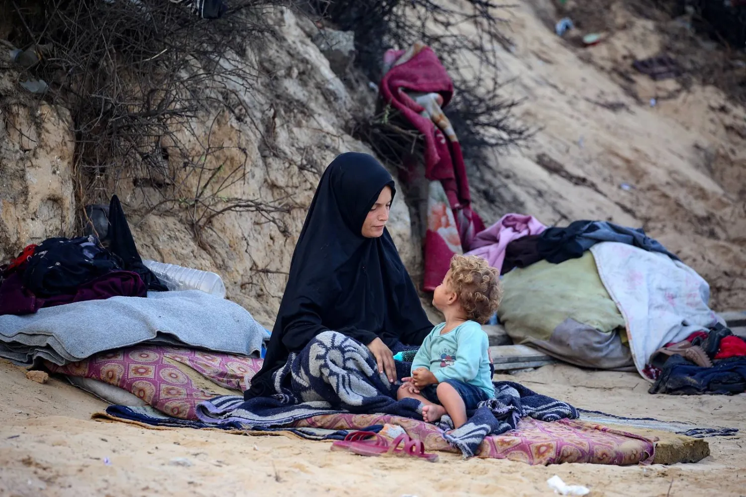 فلسطينية وطفلها فرّا من مدينة غزة يجلسان بالقرب من أمتعتهما في مخيم النصيرات للاجئين وسط قطاع غزة (أ.ف.ب)