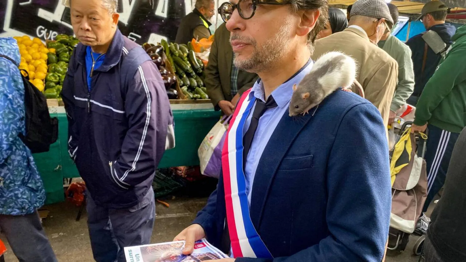The rat "Plume" sits on the shoulder of Gregory Moreau, the deputy mayor of Paris's 11th district, as he strolls through a market in the Belleville neighborhood in Paris on September 16, 2025. (AFP) 