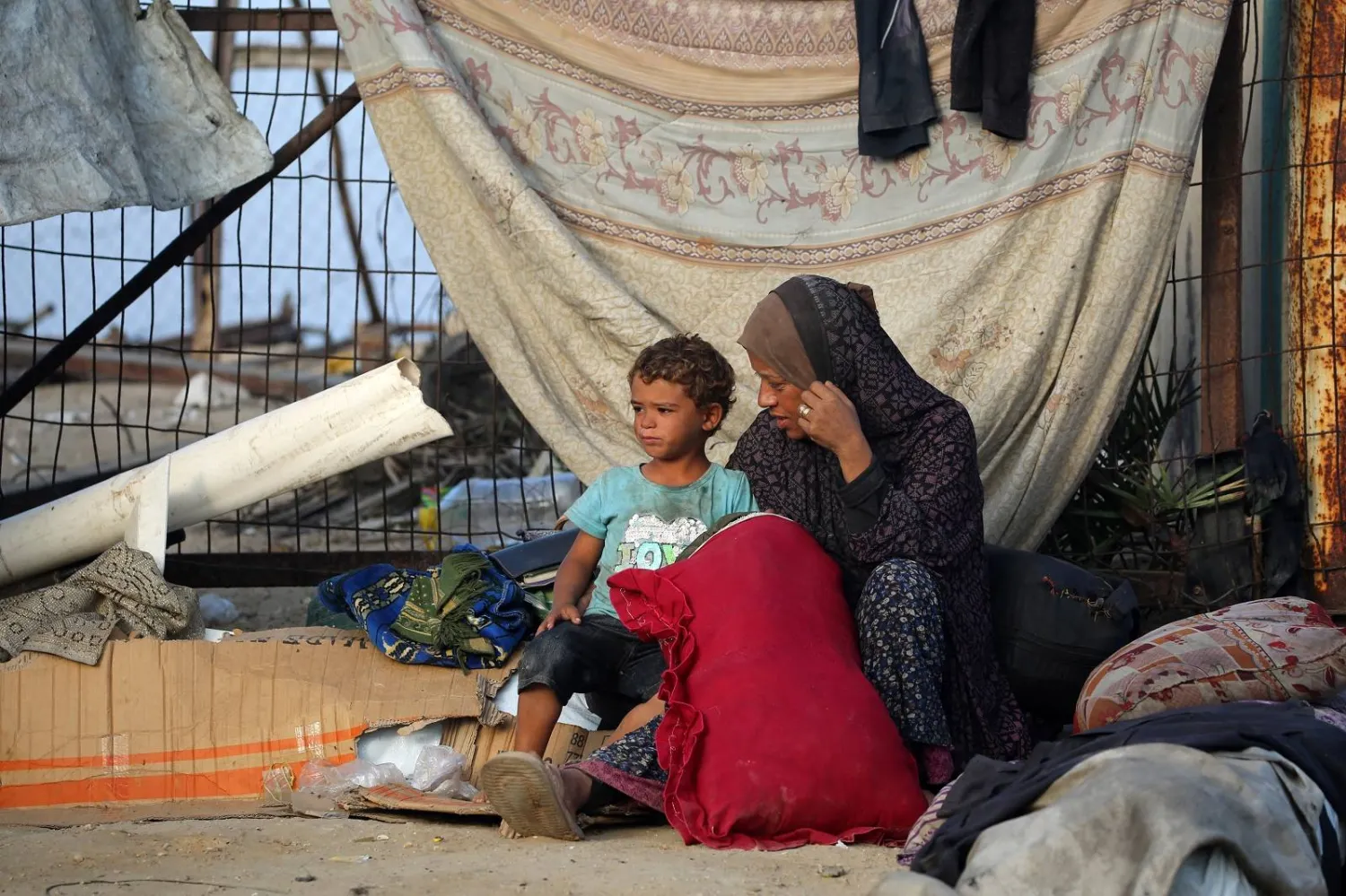 فلسطينية وطفلها فرّا من مدينة غزة يجلسان بالقرب من أمتعتهما في مخيم النصيرات للاجئين وسط غزة (أ.ف.ب)