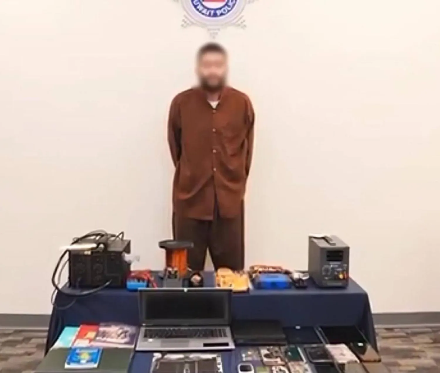 المتهم الـ«داعشي» بحوزته الأجهزة والمواد المضبوطة معه (الداخلية الكويتية)