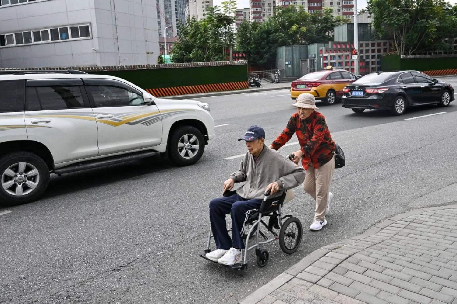 Pekin'de bir kadın, tekerlekli sandalyedeki yaşlı bir adamı sokakta gezdiriyor (AFP)