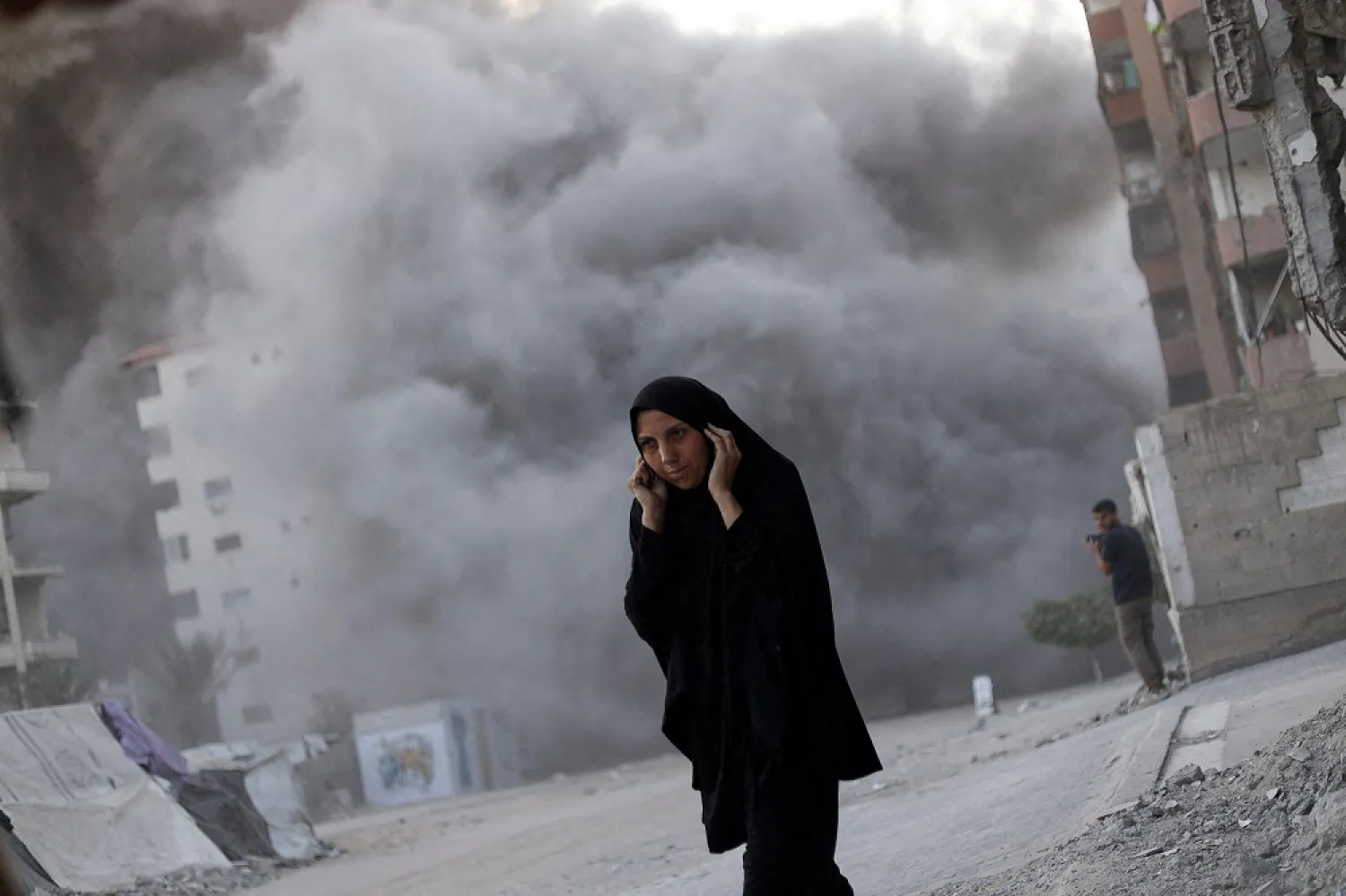 A Palestinian woman reacts as smoke rises, while a residential building collapses after an Israeli air strike, in Gaza City, September 7, 2025. (Reuters) 