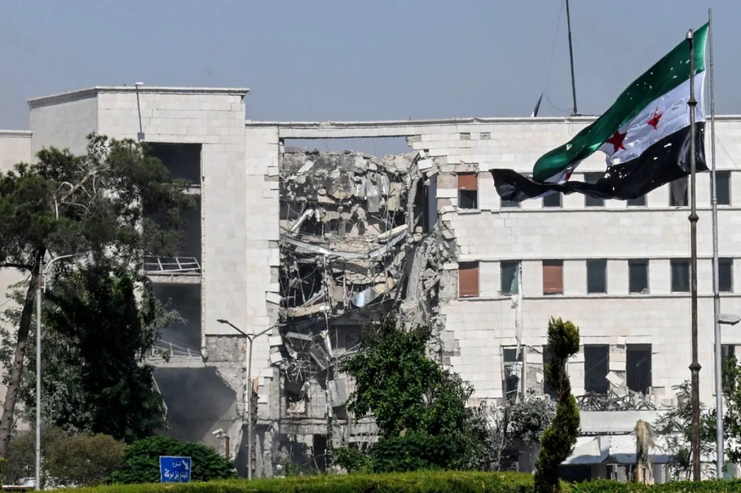 İsrail'in Şam'daki Savunma Bakanlığı merkezini bombalamasından sonra önde Suriye bayrağının parçalanmış halde görüldüğü bir fotoğraf (AFP)
