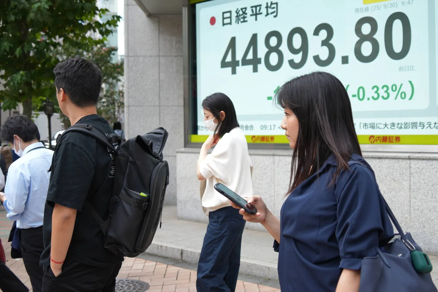 مشاة يسيرون أمام لوحة إلكترونية تعرض حركة الأسهم في وسط العاصمة اليابانية طوكيو (أ.ب)