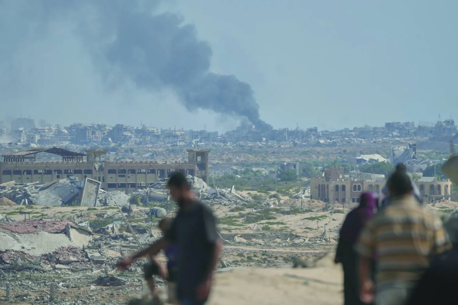 نازحون فلسطينيون يشاهدون الدخان المتصاعد من مدينة غزة بعد غارة إسرائيلية يوم الخميس (أ.ب)