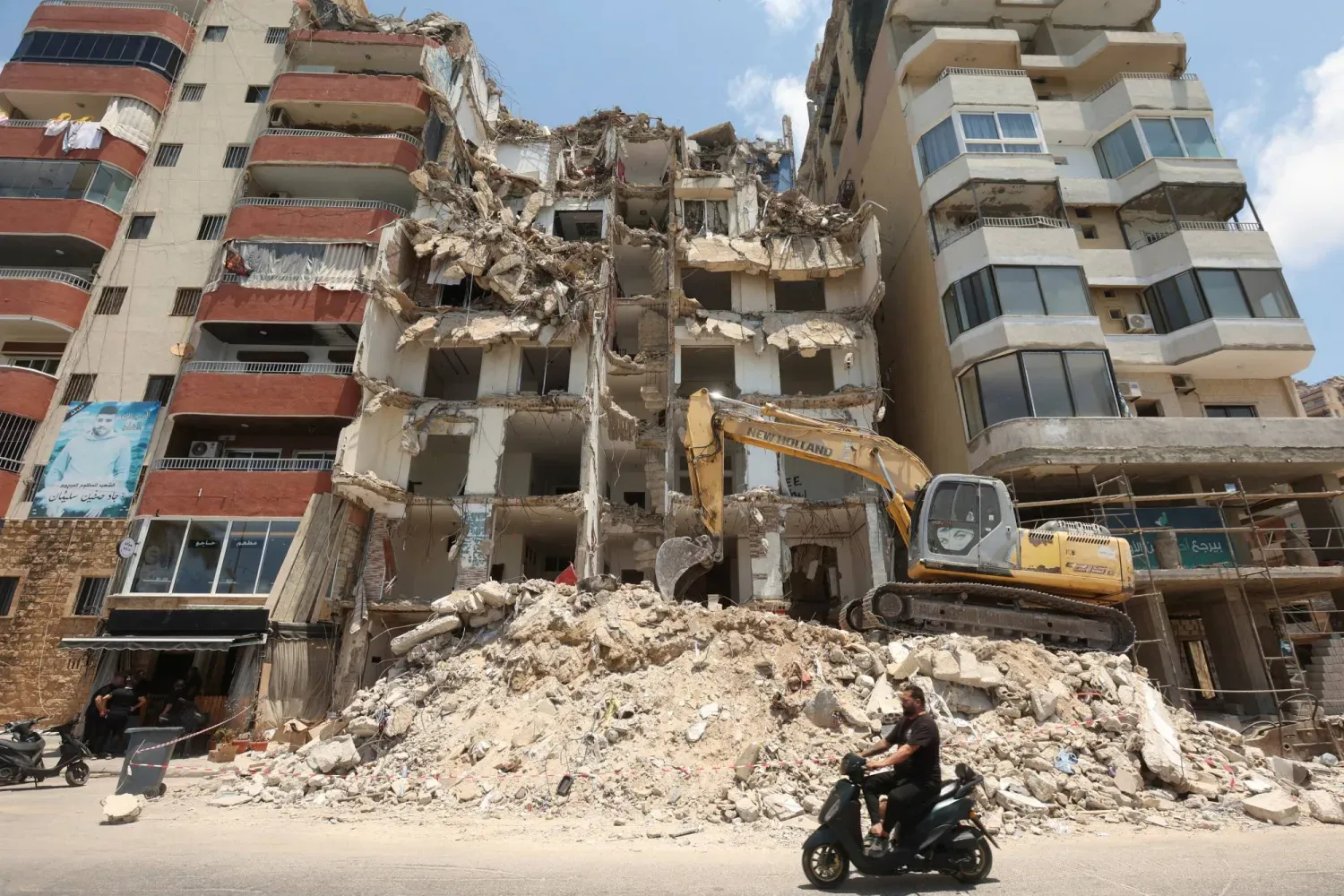 Bir adam, 3 Temmuz 2025'te Lübnan'ın güneyindeki Sur şehrine yönelik İsrail bombardımanında hasar gören bir binanın yanından motosikletiyle geçiyor. (Reuters)