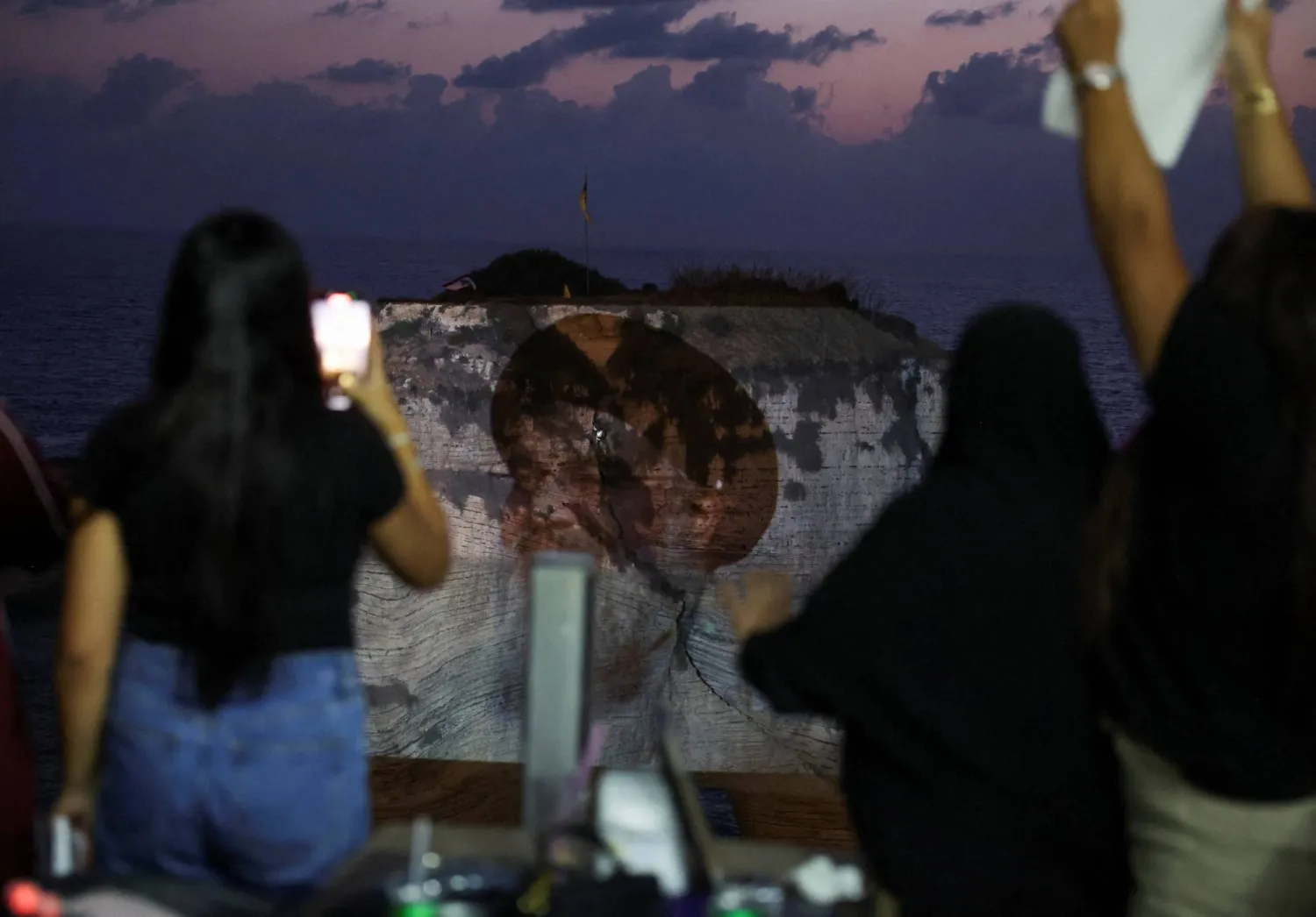 مناصرات لـ«حزب الله» يتابعن إضاءة صخرة الروشة بصورة حسن نصر الله في ذكرى اغتياله (رويترز)