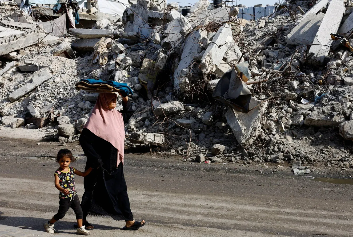 Filistinliler, İsrail'in önceki hava saldırılarında yıkılan bir konut binasının önünden geçiyor (Reuters)