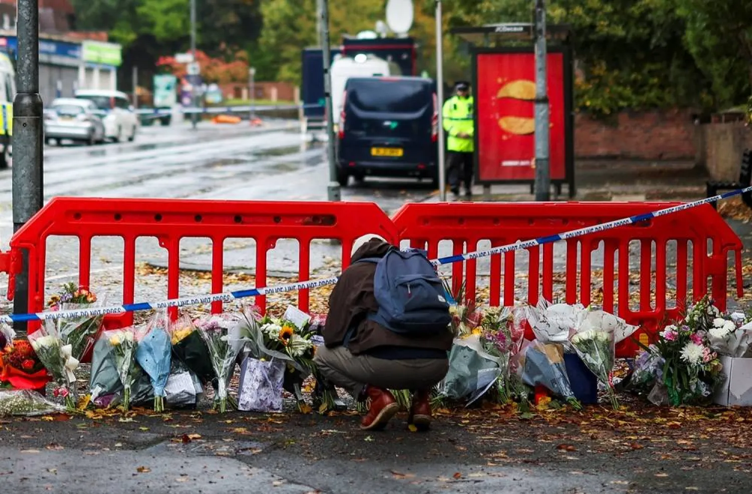 A person crouches next to floral tributes left near the Manchester synagogue in north Manchester, Britain, October 4, 2025. (Reuters)