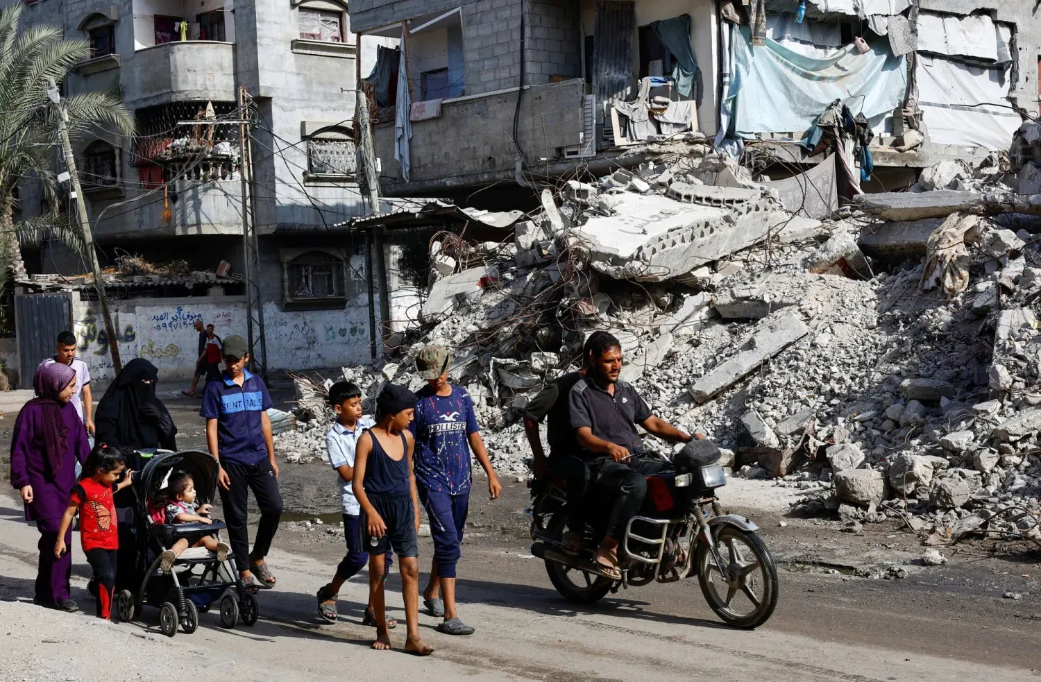 Filistinliler, Gazze Şeridi'nin merkezinde daha önce İsrail tarafından düzenlenen hava saldırılarında yıkılan bir konut binasının önünden geçiyor (Reuters)