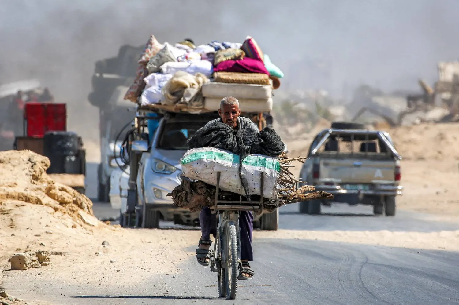 فلسطيني يركب دراجة هوائية حاملاً أخشاباً على طول الطريق الساحلي الذي يسلكه النازحون جنوباً من مدينة غزة (أ.ف.ب)