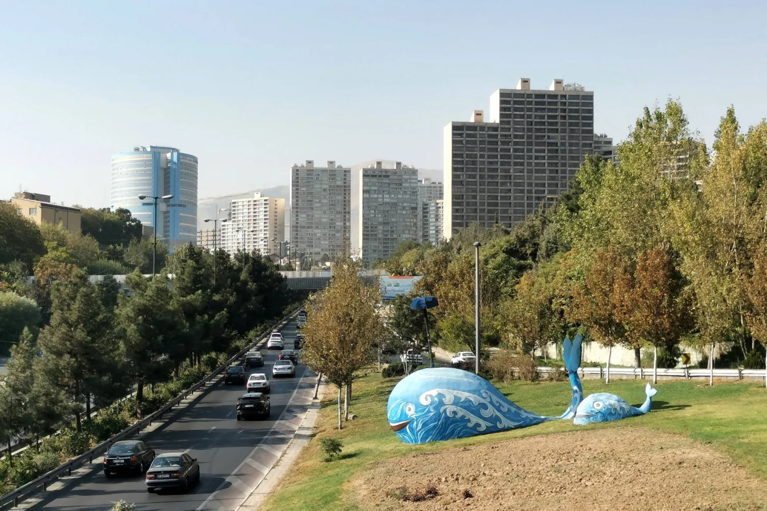 Sculptures in the shape of whales stand near a road as commuters drive toward high rise buildings in Tehran in October 4, 2025. (Photo by ATTA KENARE / AFP)