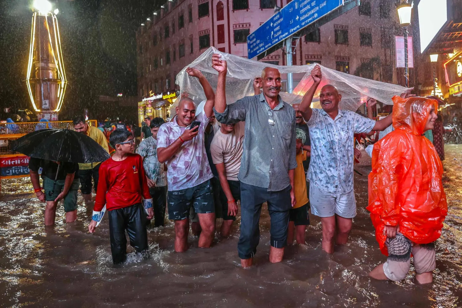 مجموعة من الأفراد يرفعون قطعة كبيرة من البلاستيك لتقيهم المطر في شمال شرق الهند (أ.ف.ب)