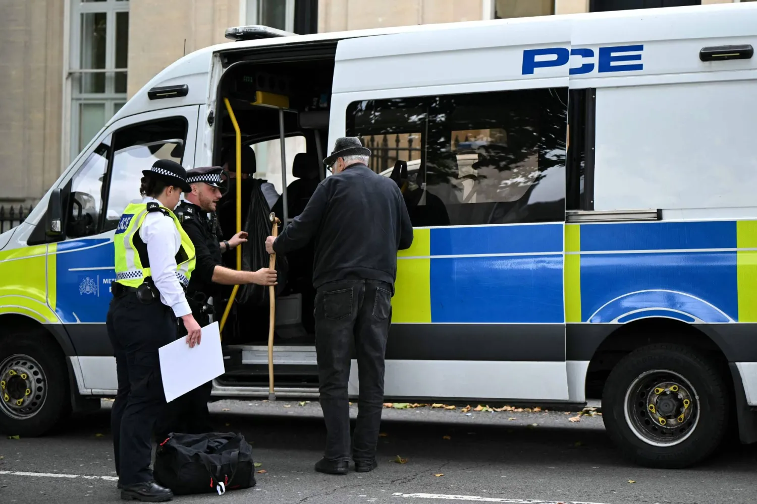 A protester hands over a walking stick before stepping into a police van at a "Lift The Ban" demonstration in support of the proscribed group Palestine Action, calling for the recently imposed ban to be lifted, in Trafalgar Square, central London, on October 4, 2025. (Photo by JUSTIN TALLIS / AFP)