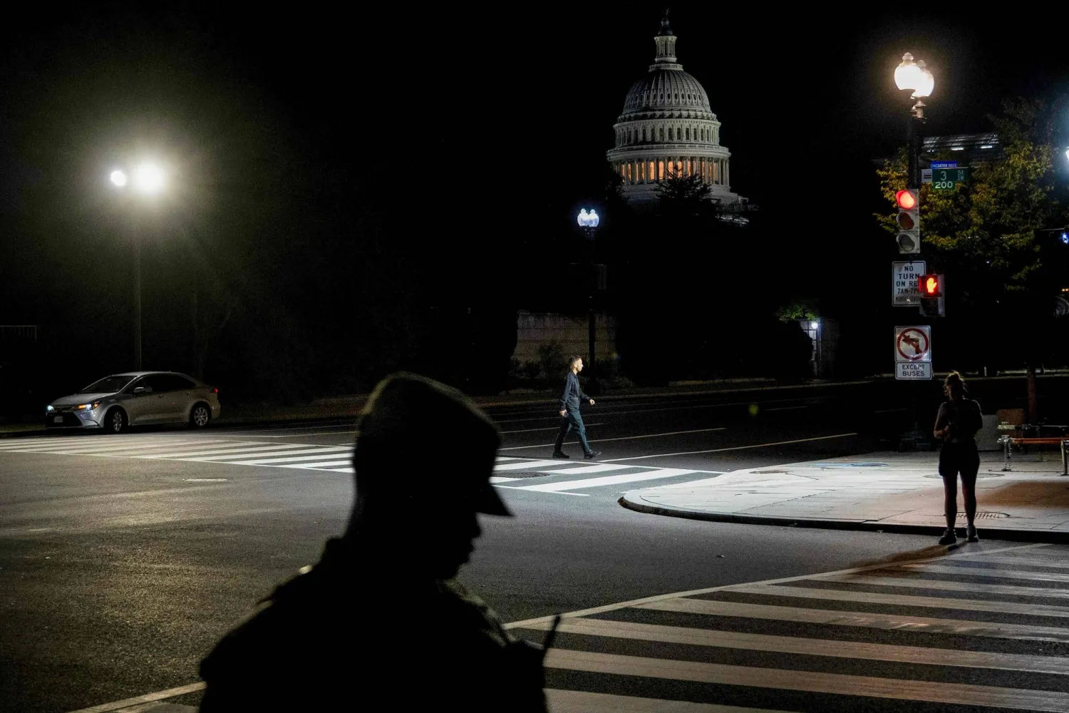 The US Capitol looms in the distance as a man crosses Independence Avenue and a member of the National Guard walks close by, on the second day of the US government shutdown in Washington, DC, on October 2, 2025. (Photo by Brendan Smialowski / AFP)