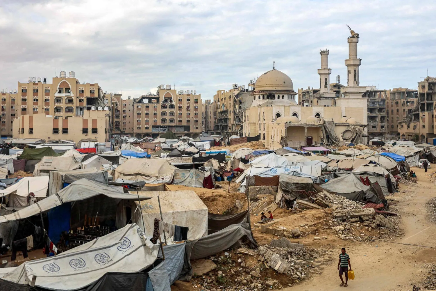 رجل يحمل وقوداً أثناء مروره بخيام لنازحين جراء الحرب قرب مسجد الشيخ حمد بن خليفة آل ثاني المتضرر بشدة شمال غربي خان يونس (أ.ف.ب)