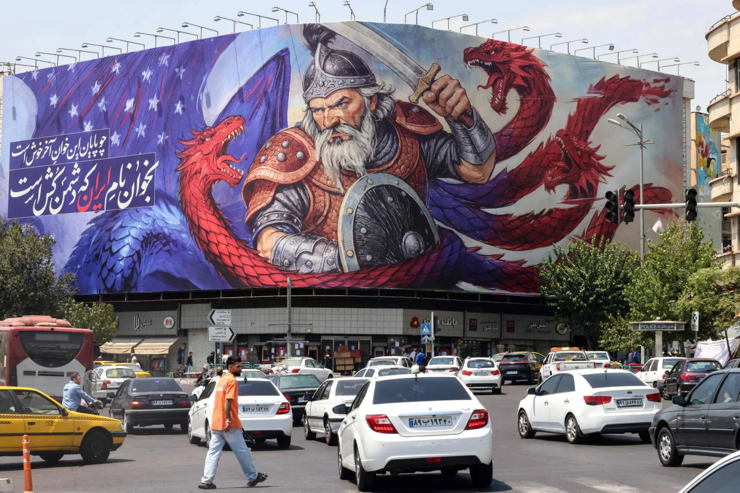 لوحة دعائية مستوحاة من الأساطير الفارسية تُصوّر رجلاً يصارع تنيناً بألوان العَلم الأميركي وقد كُتب عليها «أنشد اسم إيران التي تقتل الأعداء» وذلك في ساحة انقلاب (الثورة) وسط طهران (إ.ب.أ)