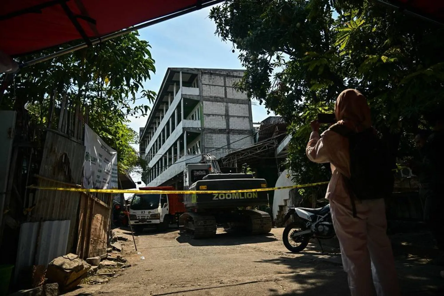 A woman takes a picture in front of the collapsed Al Khoziny Islamic boarding school in Sidoarjo, East Java, on October 6, 2025, as recovery efforts continue. (AFP)