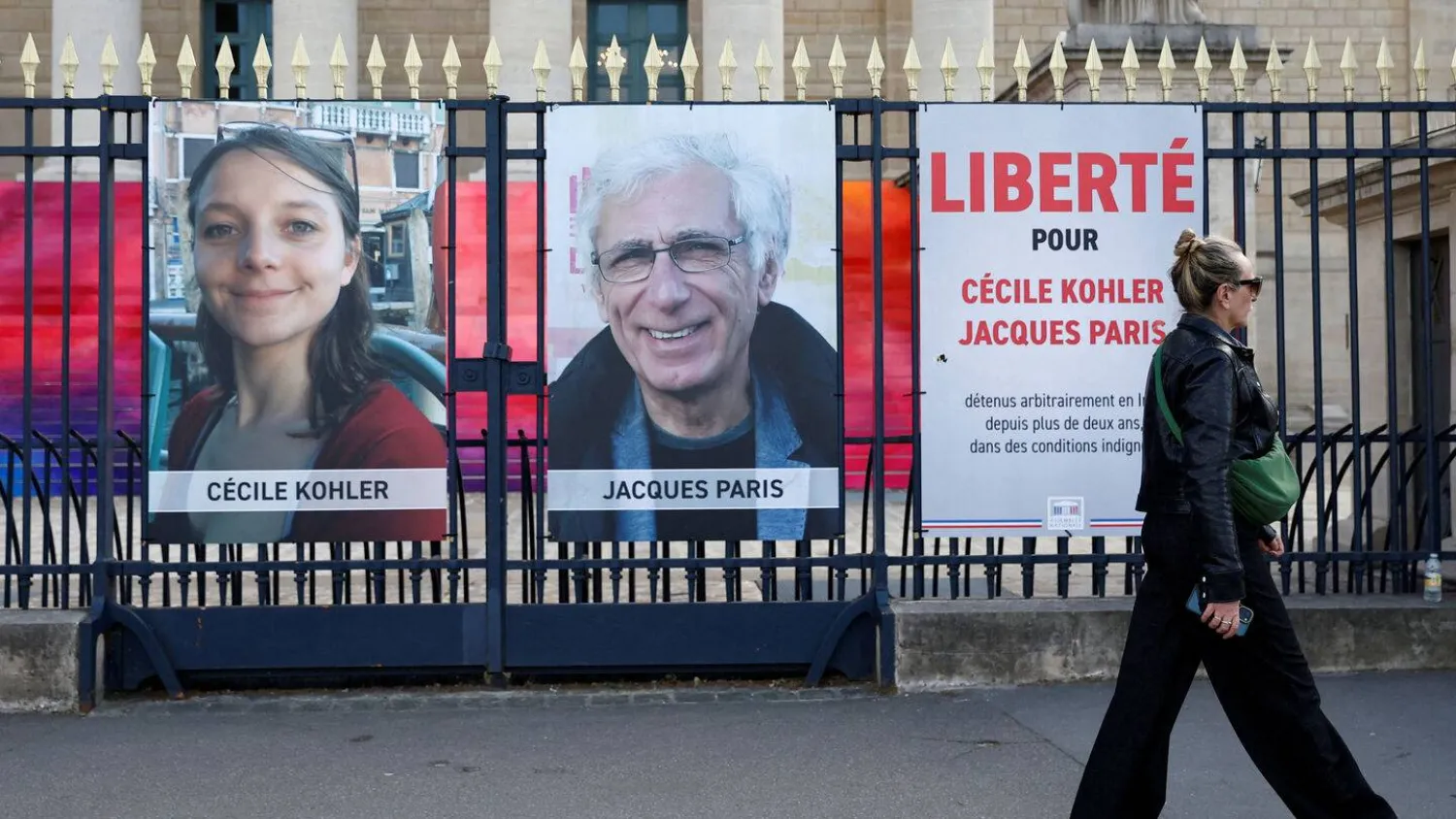 A woman walks past posters with the portraits of Cecile Kohler and Jacques Paris, two French citizens held in Iran, in front of the National Assembly in Paris, France, May 7, 2025. (Reuters) 