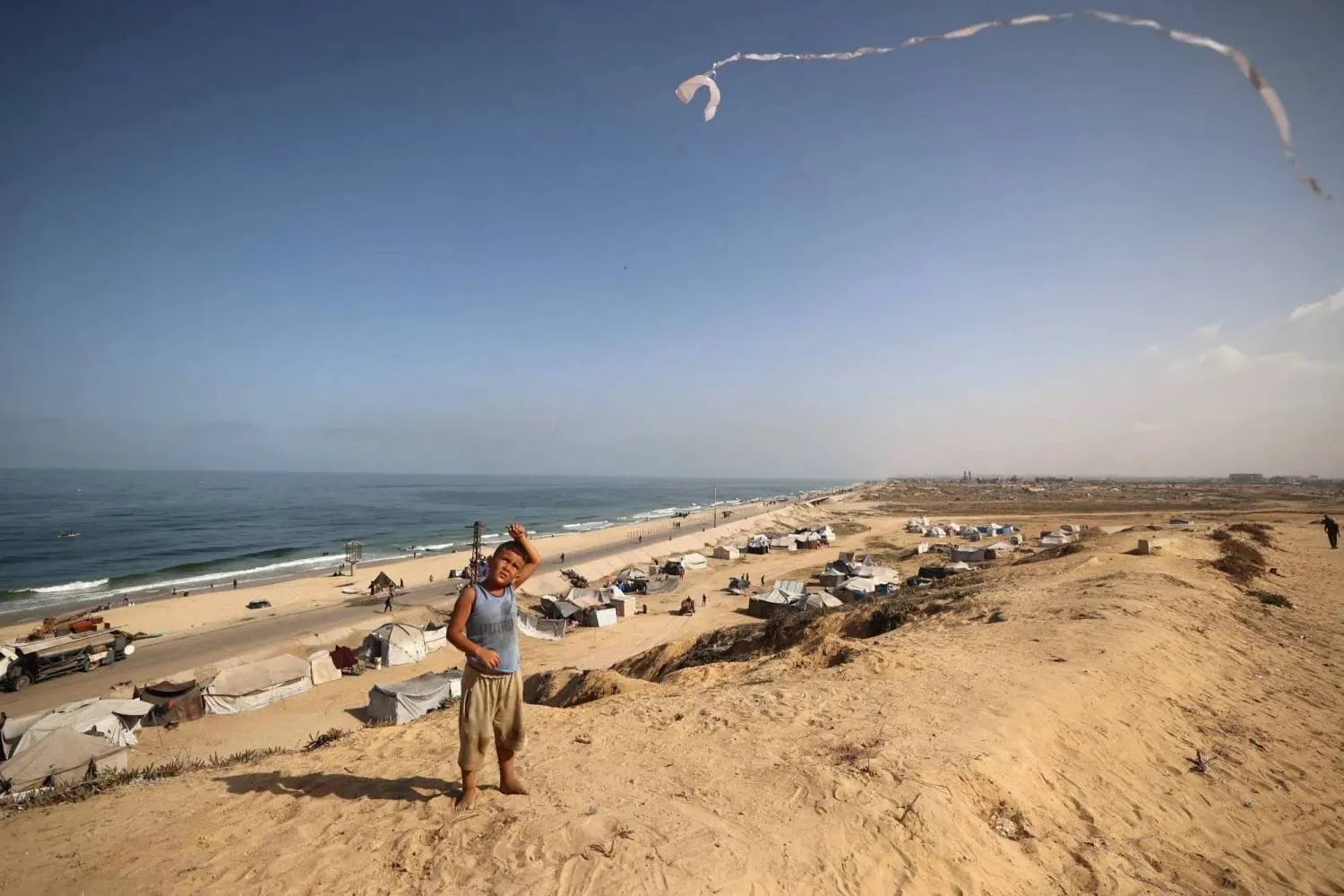 A Palestinian boy flies his kite near tents of displaced families in the Nuseirat camp, in the central Gaza Strip (AFP). 
