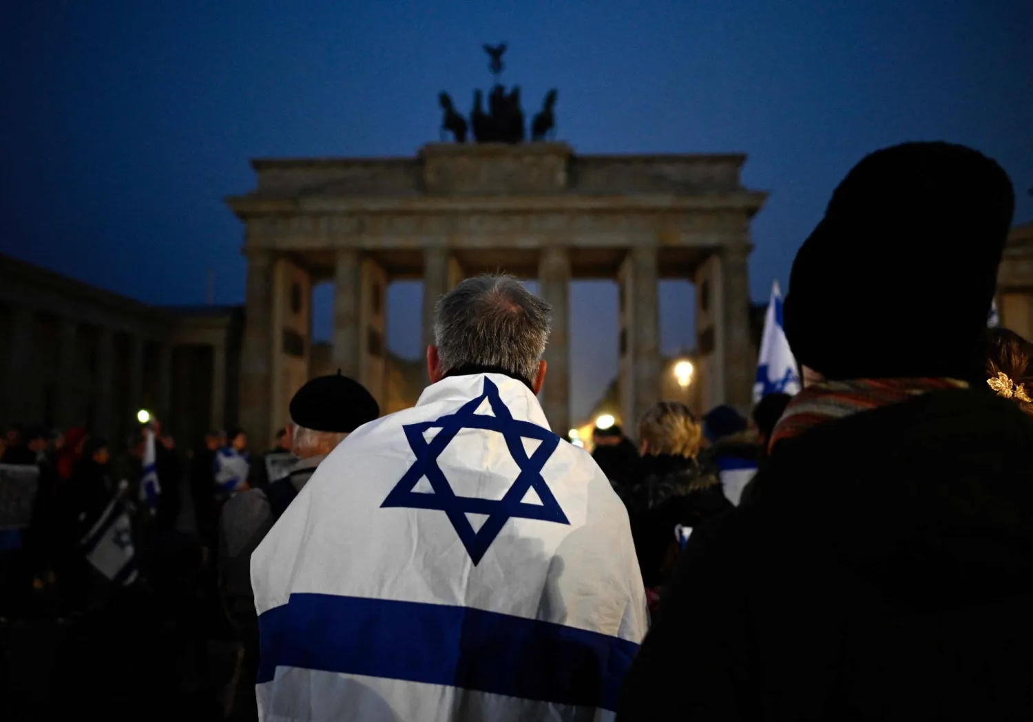 A man wrapped in an Israeli flag attends a vigil to remember the victims of the Hamas attack in front of Brandenburg gate in Berlin on early October 7, 2025, the second anniversary of the Hamas' October 7, 2023 attack on Israel. (AFP)