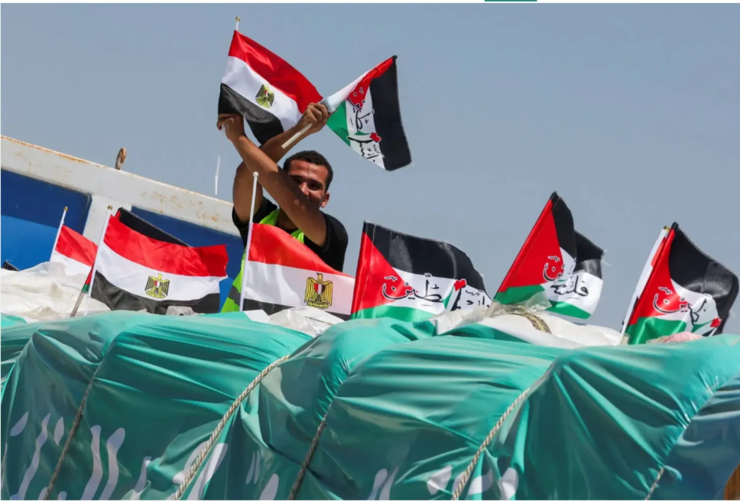 شخص يحمل العلمين المصري والفلسطيني على شاحنة تحمل مساعدات إنسانية بالقرب من معبر رفح (رويترز)