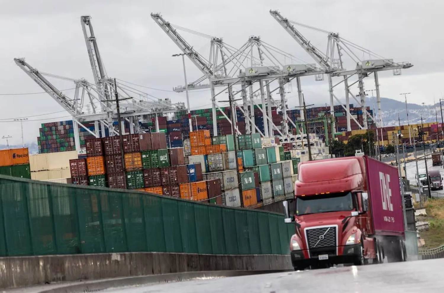 شاحنة تمر أمام حاويات شحن في ميناء أوكلاند بكاليفورنيا (رويترز)
