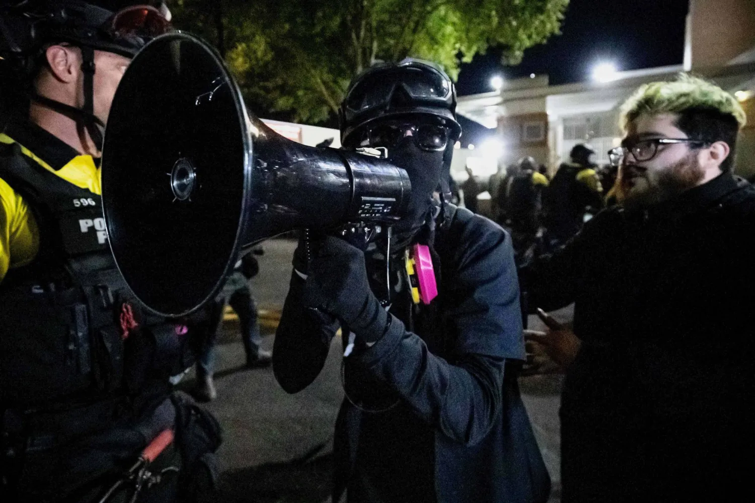 متظاهر يصرخ عبر ميكروفون في وجه مؤيدين للرئيس الأميركي دونالد ترمب خارج منشأة تابعة لدائرة إنفاذ قوانين الهجرة والجمارك في بورتلاند بأوريغون (أ.ب)