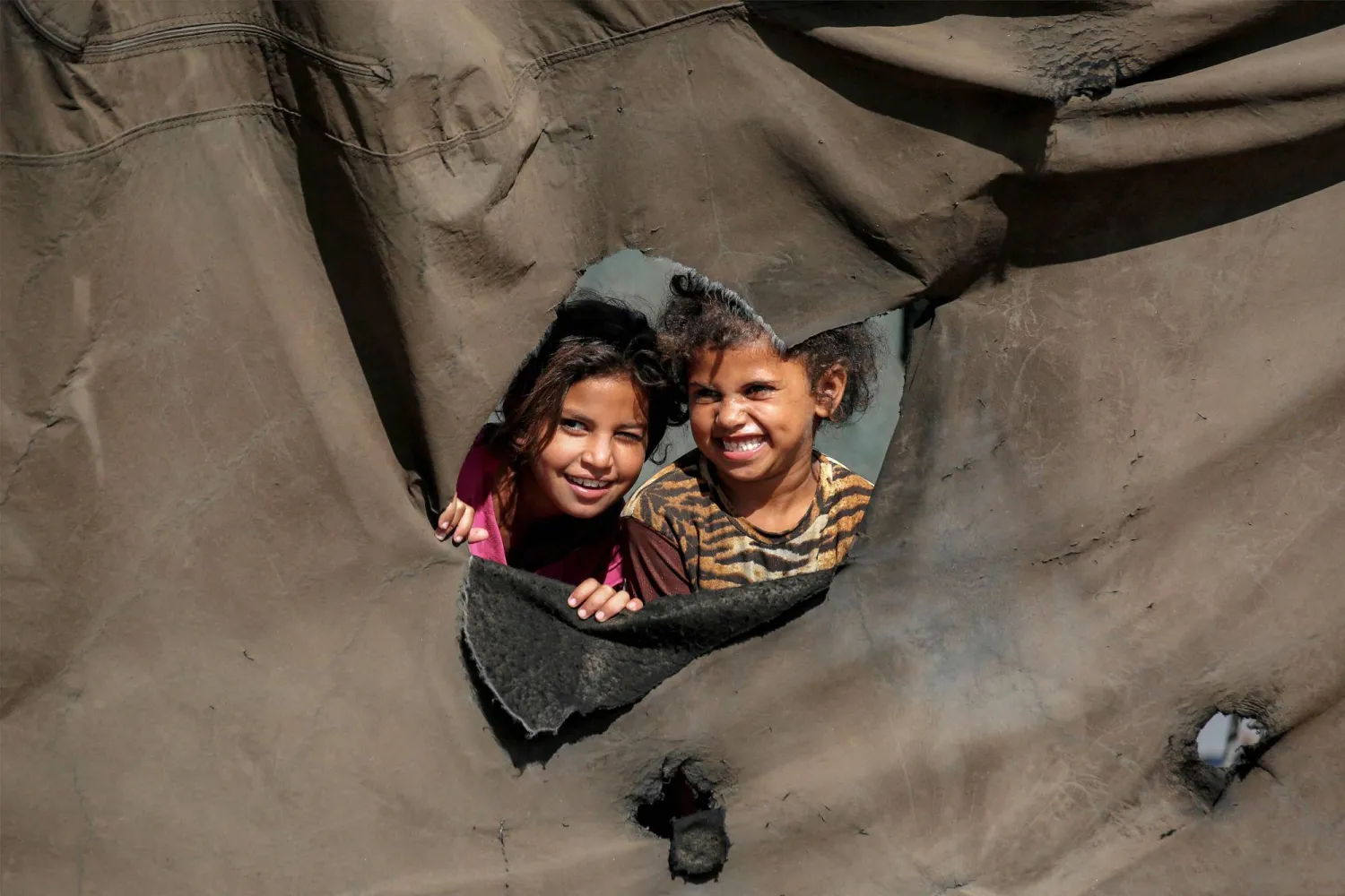 طفلتان تنظران من ثقب في خيمة نازحين بالنصيرات وسط قطاع غزة الثلاثاء (أ.ف.ب)