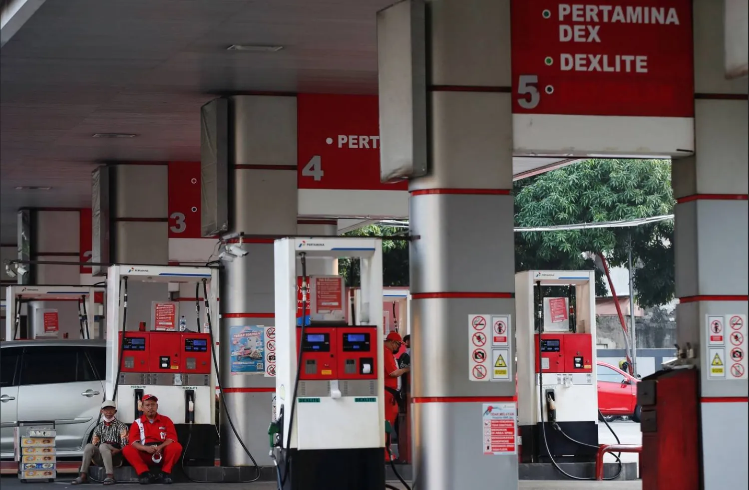 عامل يجلس مع بائع متجول أثناء انتظاره الزبائن بمحطة وقود تابعة لشركة بيرتامينا المملوكة للدولة في جاكرتا بإندونيسيا (رويترز)