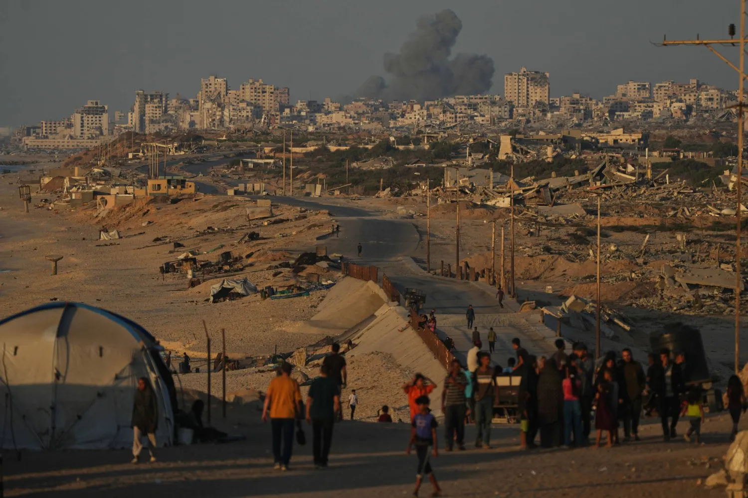 Displaced Palestinians walk along the coastal road, backdropped by smoke rising into the sky after an Israeli military strike in Gaza City, as seen from the central Gaza Strip, Wednesday, Oct. 8, 2025. (AP Photo/Abdel Kareem Hana)