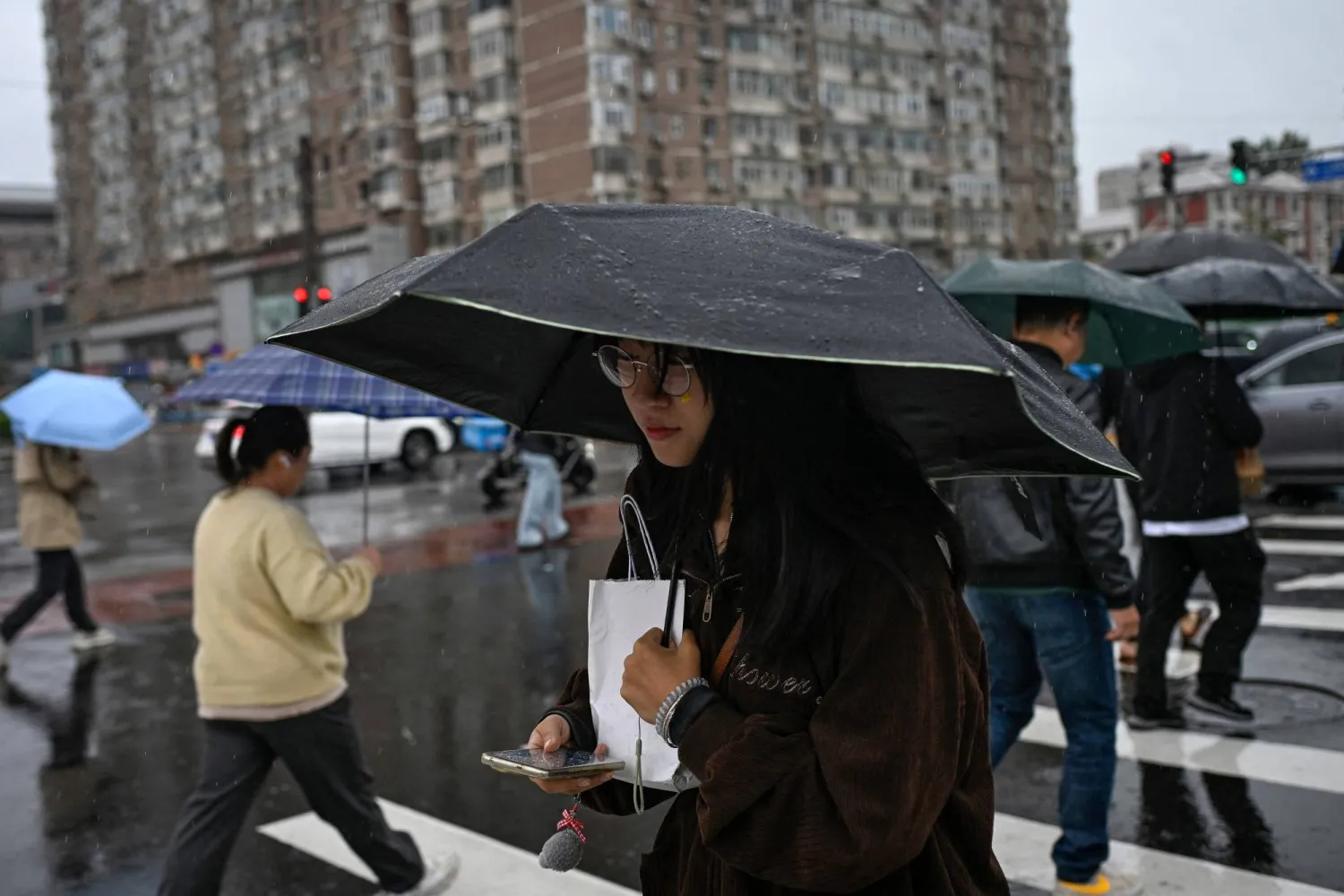 مشاة يعبرون الطريق تحت المطر في العاصمة الصينية بكين (أ.ف.ب)