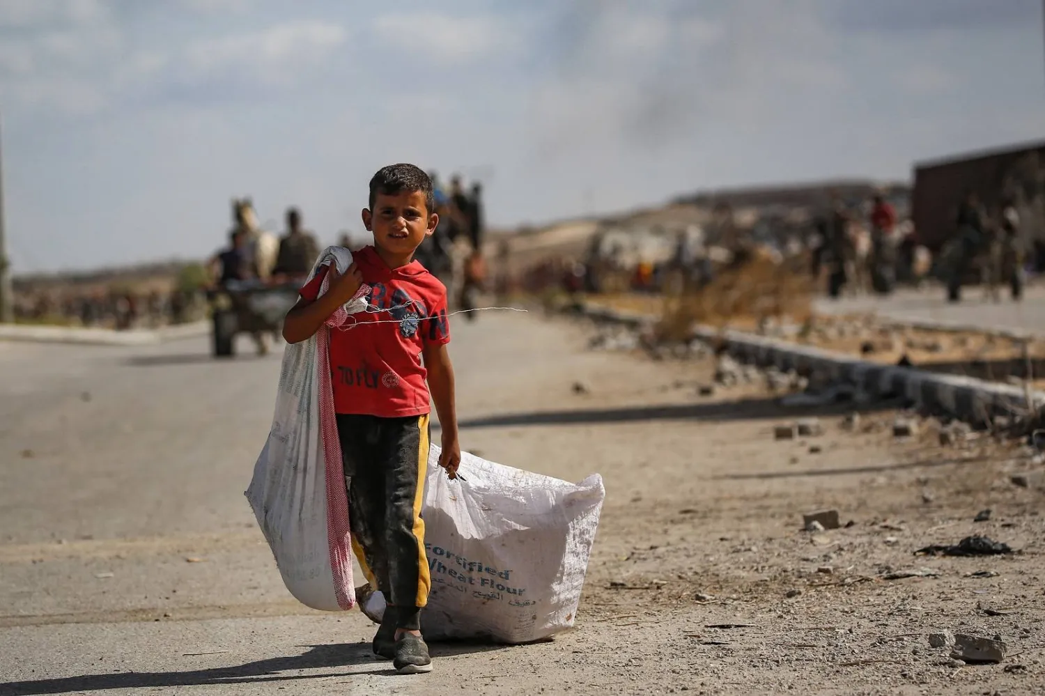 طفل فلسطيني يحمل حقيبة ويجرّ أخرى خلفه بالقرب من معبر نتساريم وسط قطاع غزة (أ.ف.ب)