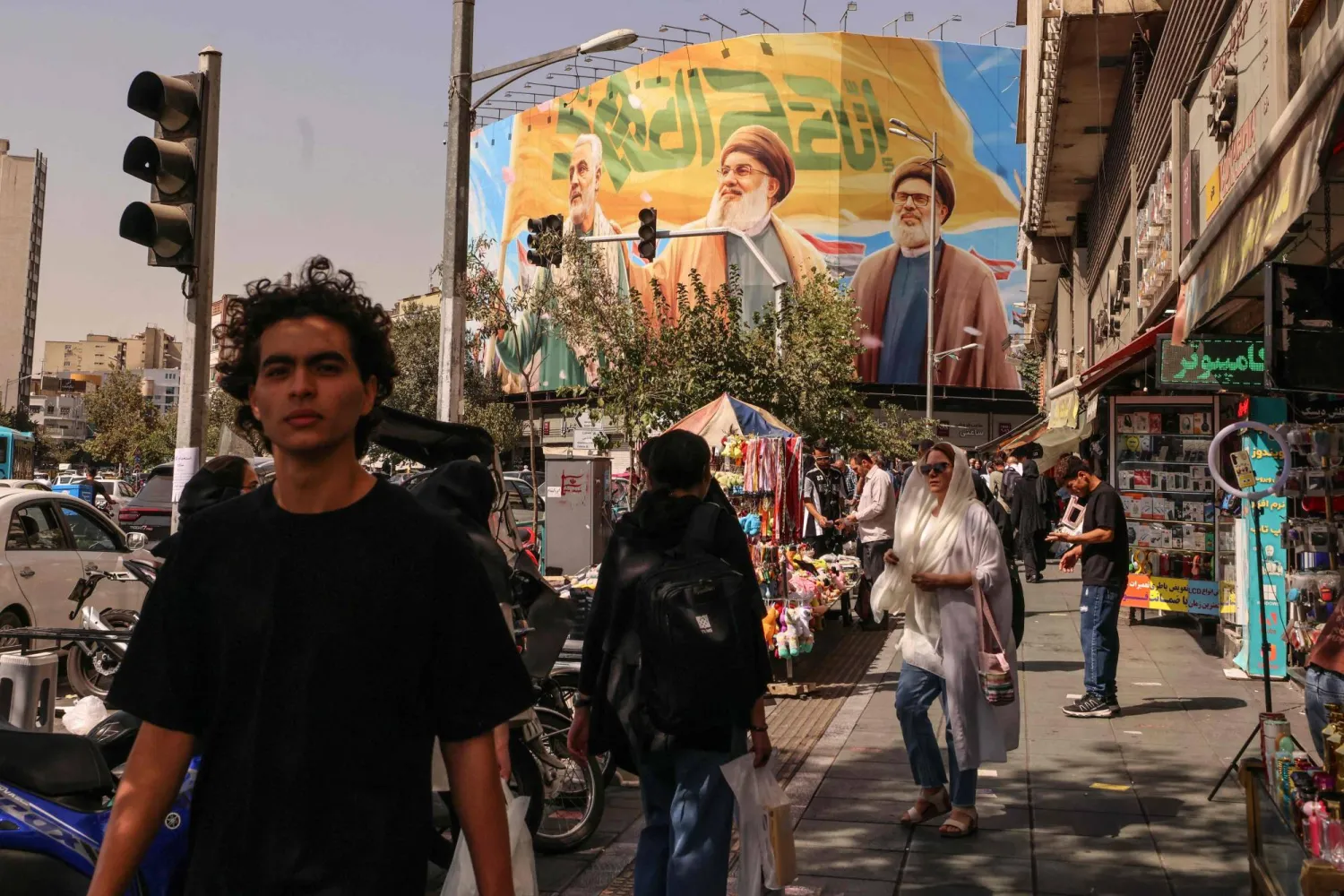 People walk in front of a billboard depicting slain Lebanese Hezbollah leaders Hassan Nasrallah (C) and his successor Hashem Safieddine (R) as well as the late Iranian General Qasem Soleimani, in Tehran on September 28, 2025. (Photo by ATTA KENARE / AFP)