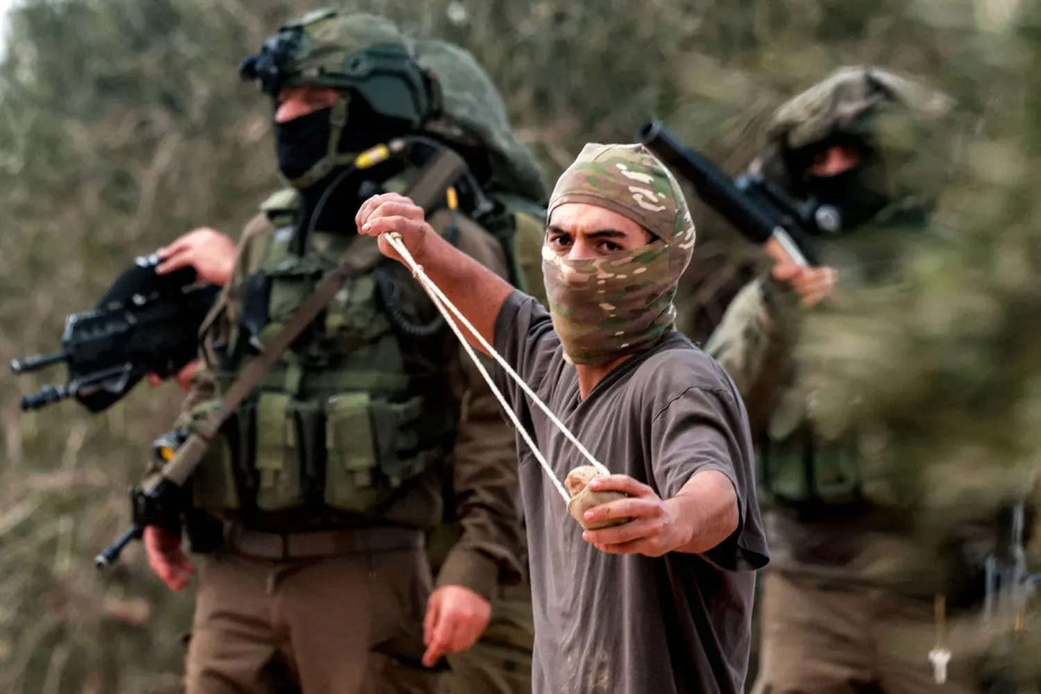 Maskeli bir yerleşimci, arkasında İsrail askerleri varken Batı Şeria'da zeytin toplayan Filistinlilere taş atıyor (AFP)
