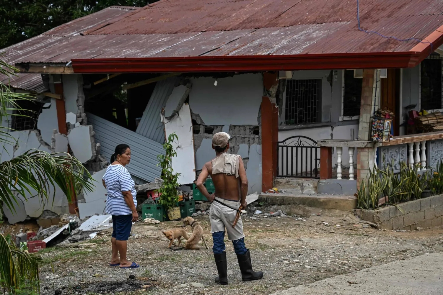 People look at a damaged house in Manay, in the province of Davao Oriental on October 11, 2025. (Photo by Jam STA ROSA / AFP)
