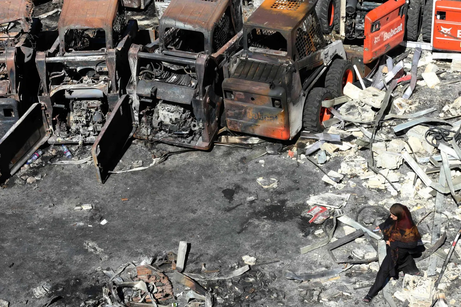 امرأة تمشي أمام مُعدات زراعية متفحمة في موقع غارة إسرائيلية ليلية على قرية المصيلح جنوب لبنان أمس (أ.ف.ب)