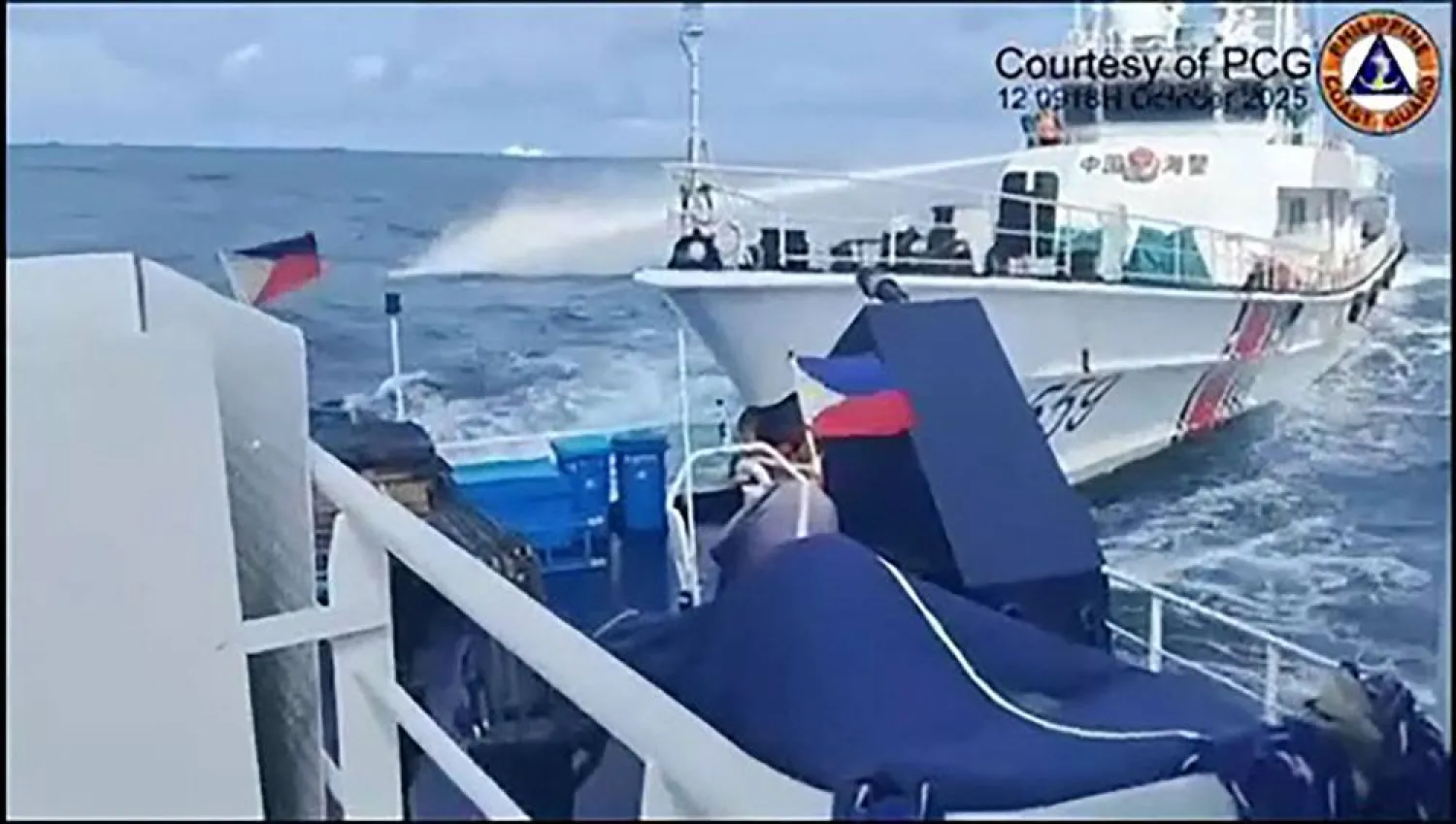 This frame grab from handout video footage taken and released on October 12, 2025 by the Philippine Coast Guard shows a China Coast Guard ship (R) deploying water cannon as seen from a Philippine Bureau of Fisheries vessel during an incident near Thitu island in disputed waters of the South China Sea. (Handout / Philippine Coast Guard (PCG) / AFP) 