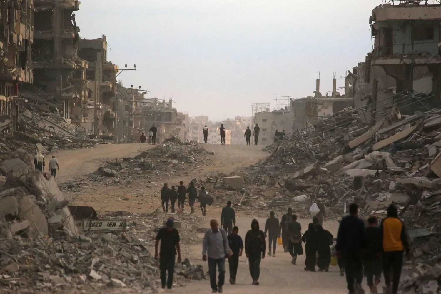 فلسطينيون يشقون طريقهم وسط المباني المدمرة مع عودتهم إلى مدينة غزة اليوم (أ.ف.ب)