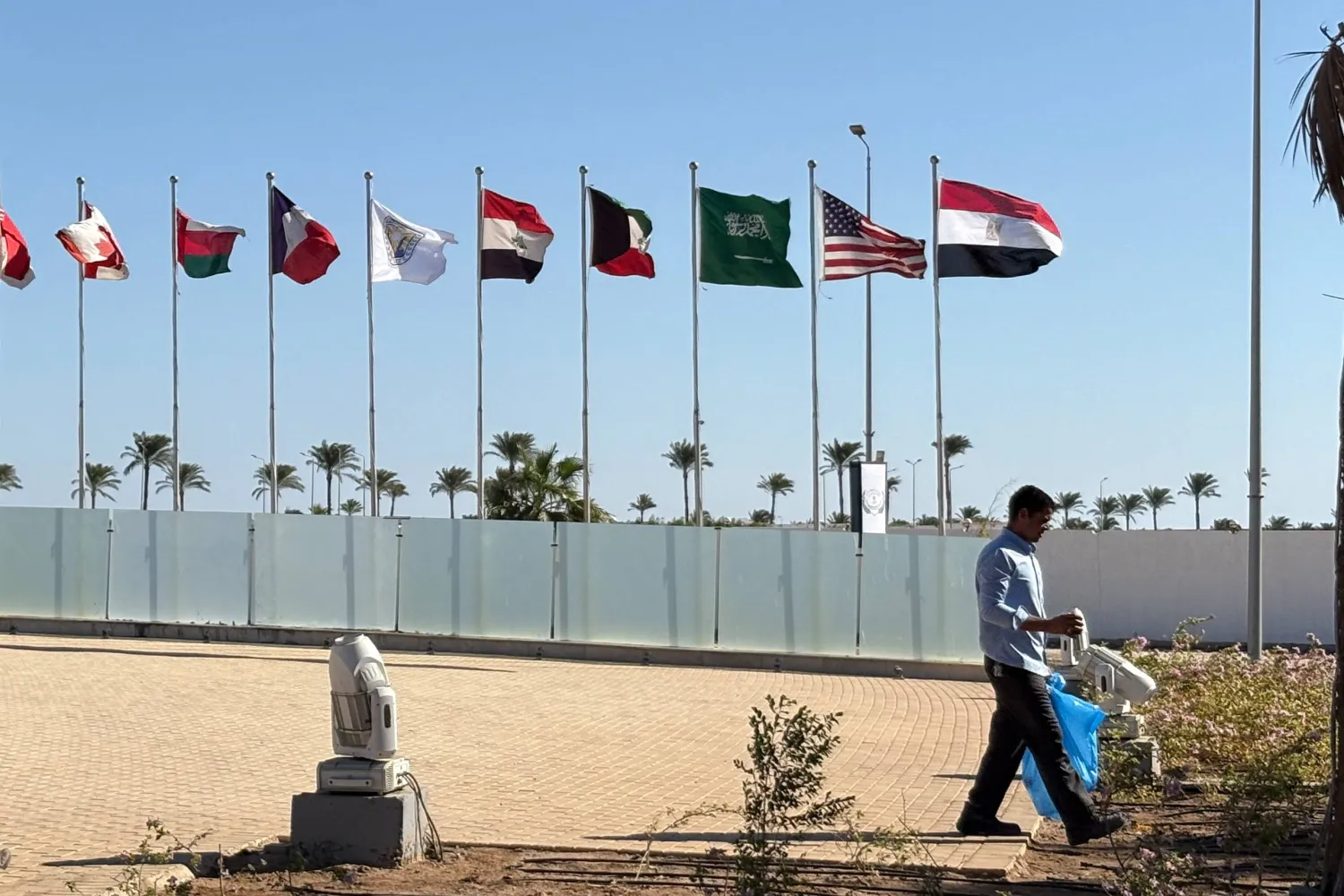 عامل يسير أمام أعلام البلدان المشاركة في قمة شرم الشيخ قبل انعقادها غداً (أ.ب)