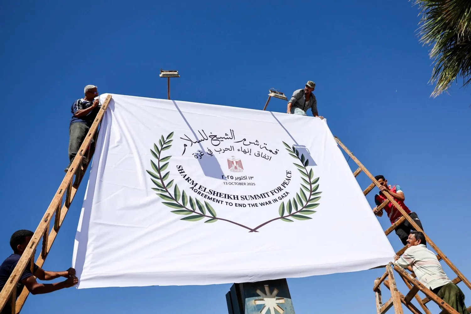عاملون مصريون يعلقون يوم الأحد إحدى اللافتات عن «قمة شرم الشيخ للسلام» التي تُعقد الاثنين (رويترز)