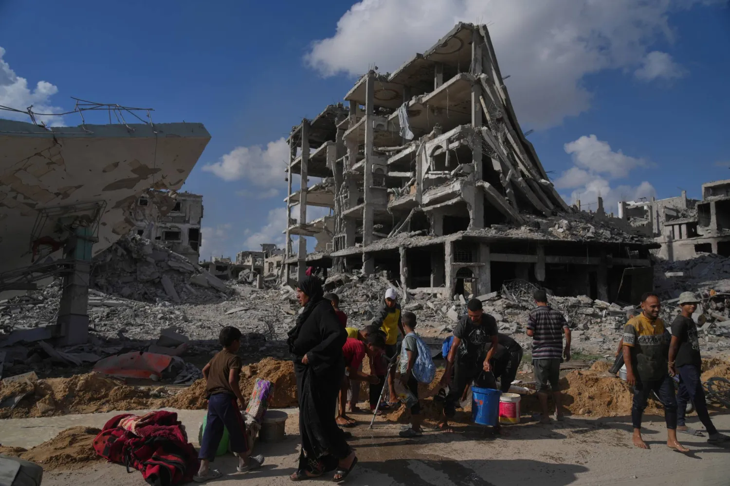 فلسطينيون يجمعون المياه من أنبوب مكسور يحيط بالمباني المدمَّرة في مدينة غزة أمس (أ.ب)