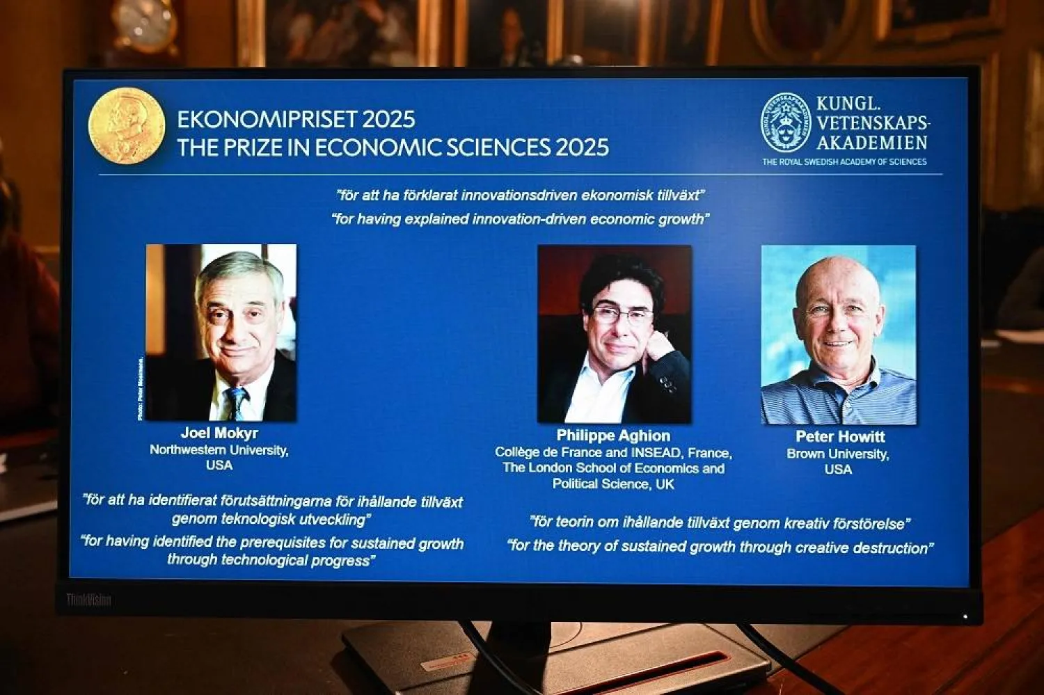 A screen displays the portraits of the 2025 prize winners (L-R) Joel Mokyr, Philippe Aghion and Peter Howitt, during the announcement of the winners of the 2025 Nobel Prize in Economics, the Sveriges Riksbank Prize in Economic Sciences in Memory of Alfred Nobel, at the Royal Swedish Academy of Sciences in Stockholm, Sweden, on October 13, 2025. (AFP)